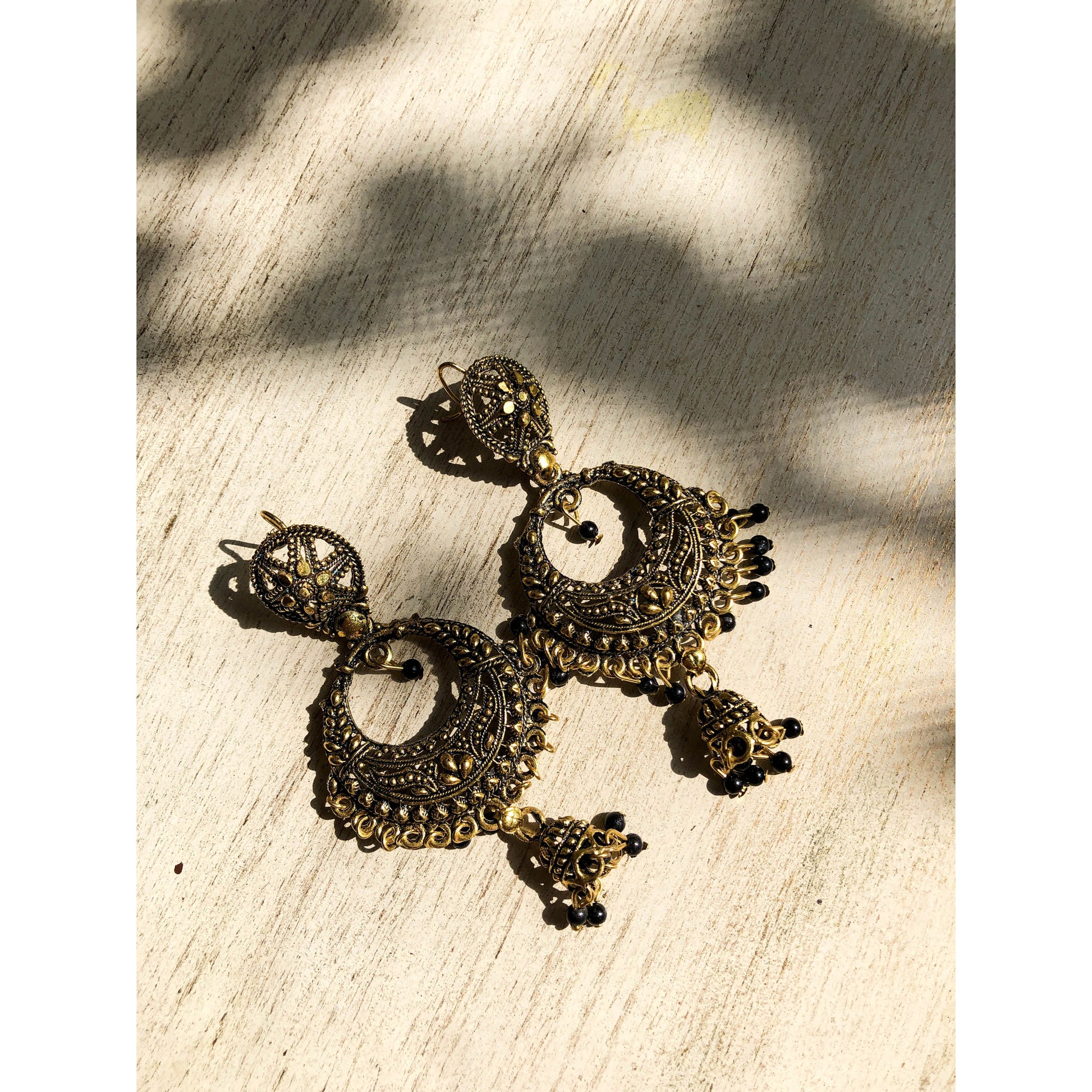 A collection of traditional jhumka earrings, featuring ornate bell shapes with intricate filigree details and various colorful accents like blue enamel or small dangling beads.