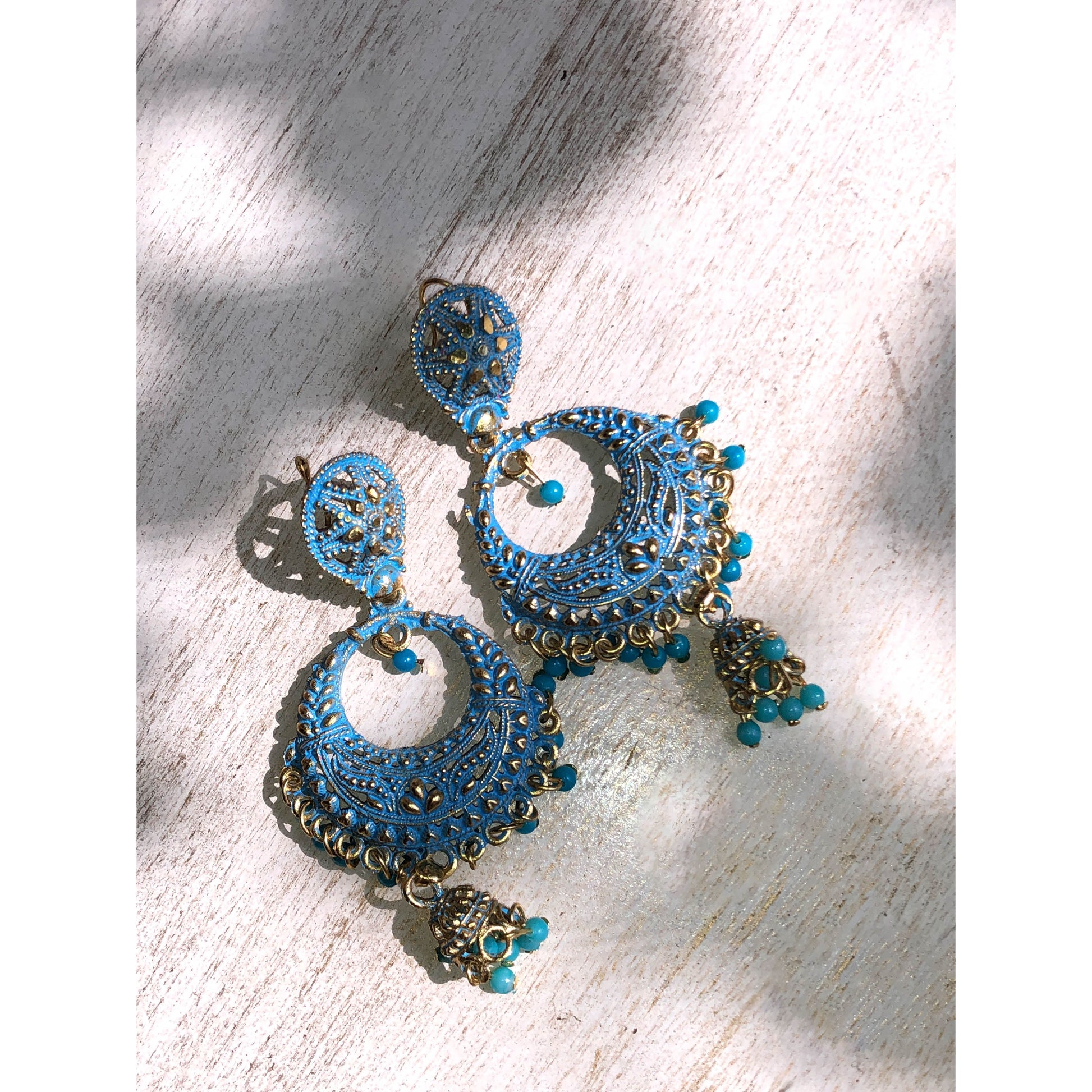 A collection of traditional jhumka earrings, featuring ornate bell shapes with intricate filigree details and various colorful accents like blue enamel or small dangling beads.