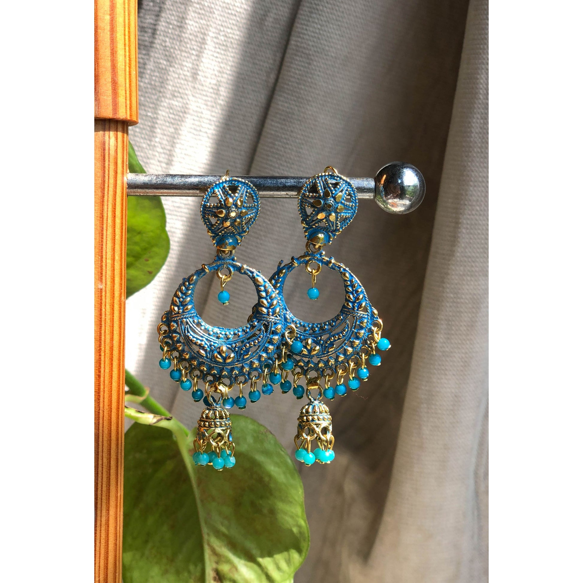 A collection of traditional jhumka earrings, featuring ornate bell shapes with intricate filigree details and various colorful accents like blue enamel or small dangling beads.