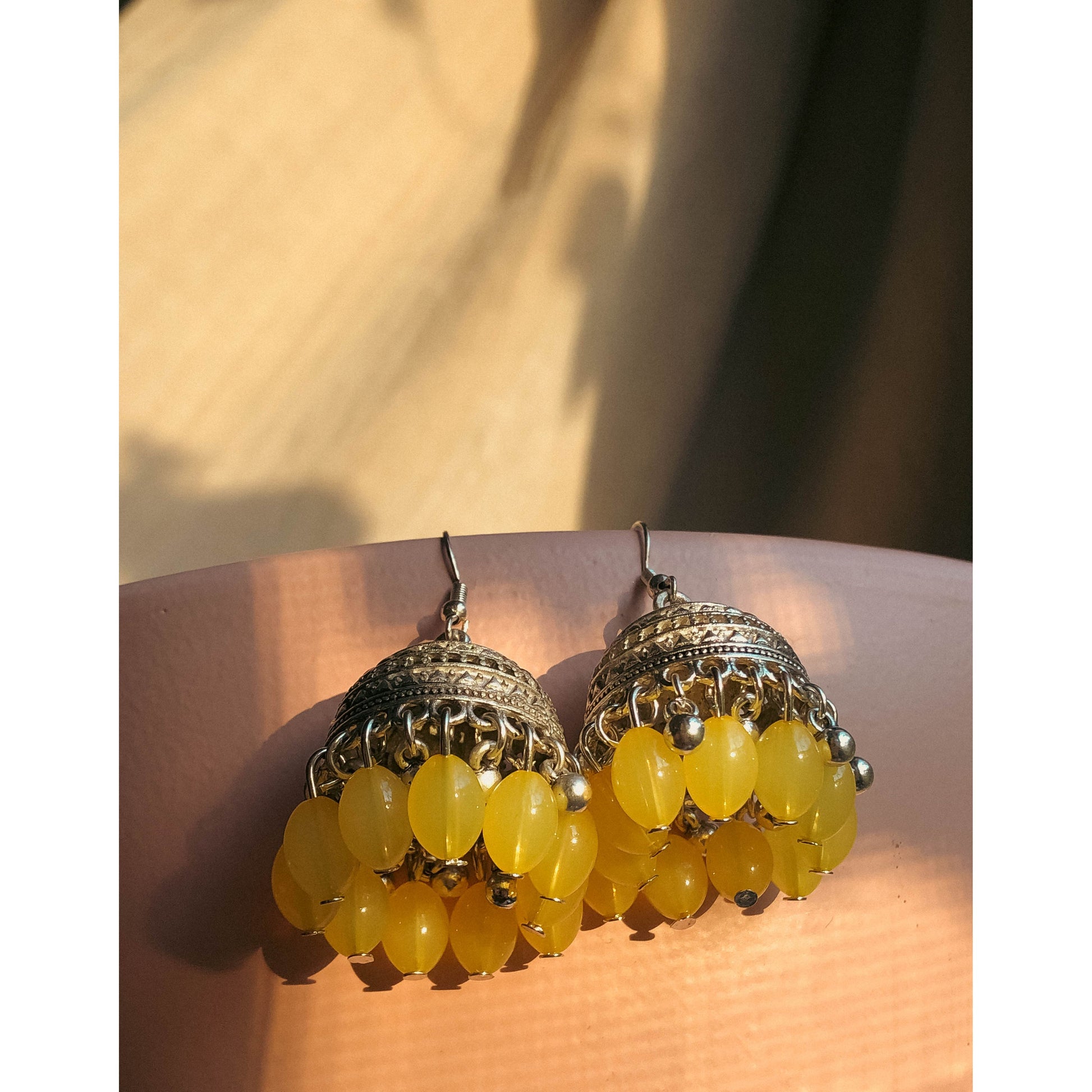 A pair of silver-tone jhumka earrings featuring a round, sparkling top section covered in clear stones, with a bell-shaped dangle below adorned with clear stones and small white pearl or bead accents