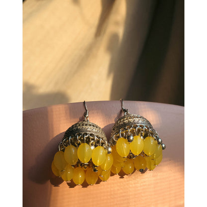 A pair of silver-tone jhumka earrings featuring a round, sparkling top section covered in clear stones, with a bell-shaped dangle below adorned with clear stones and small white pearl or bead accents