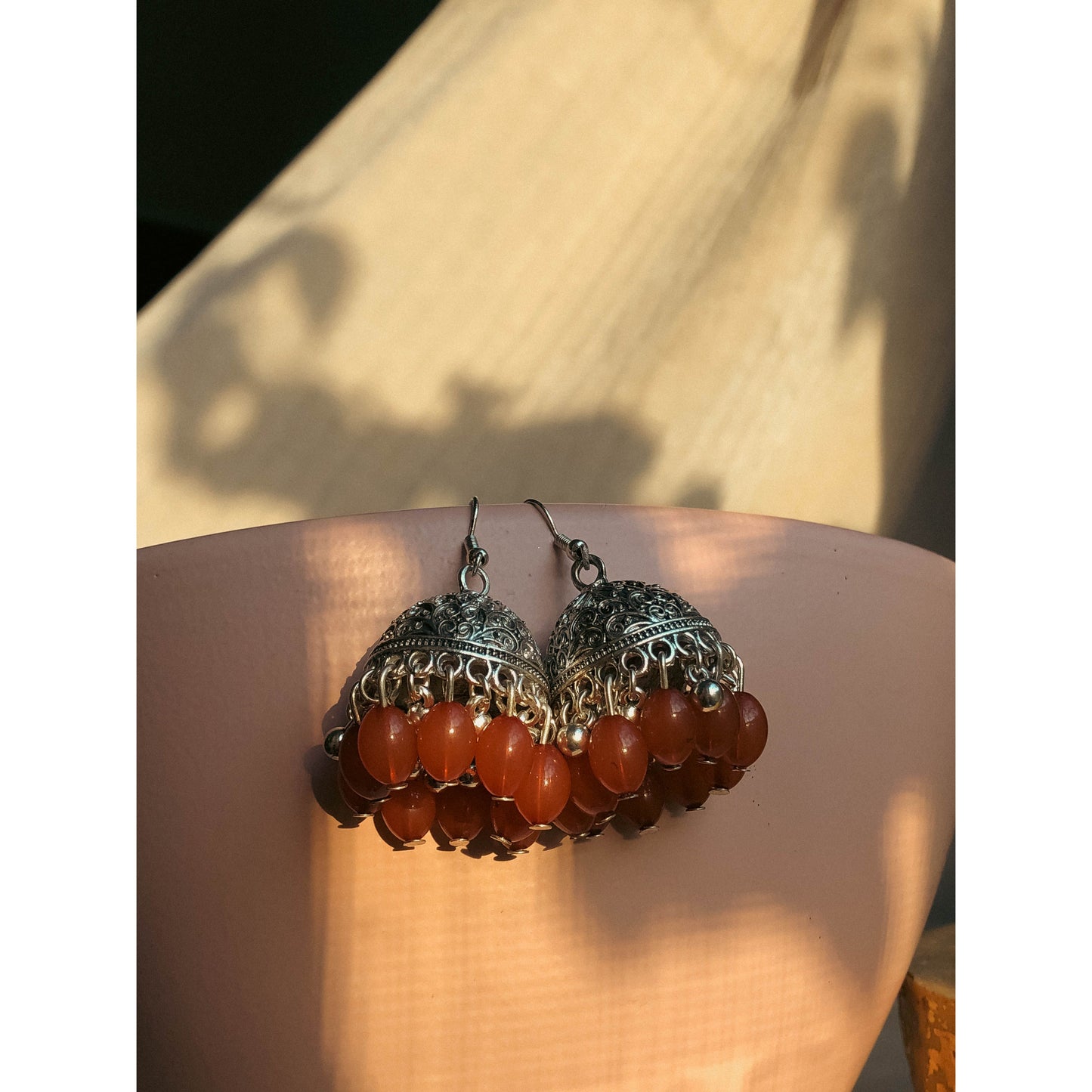 A pair of silver-tone jhumka earrings featuring a round, sparkling top section covered in clear stones, with a bell-shaped dangle below adorned with clear stones and small white pearl or bead accents