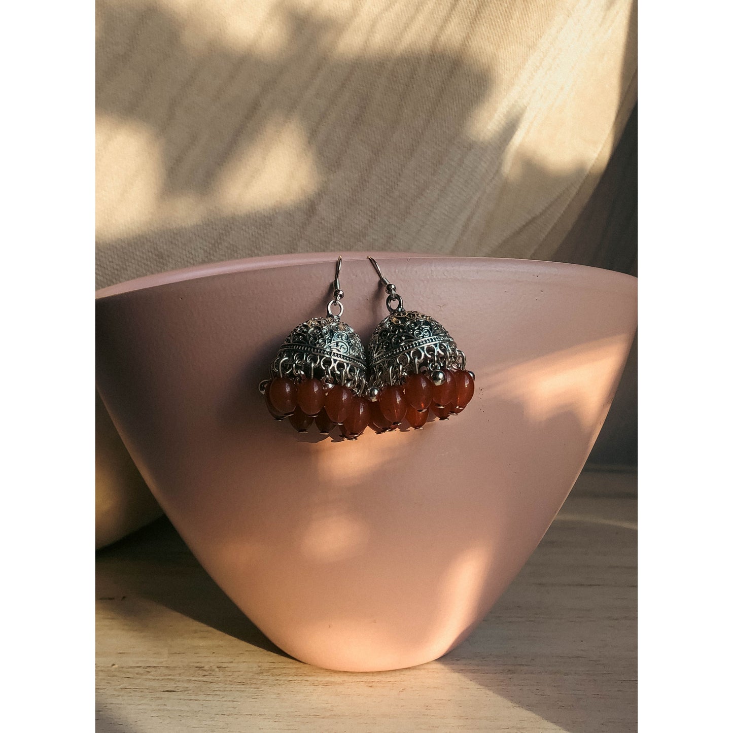 A pair of silver-tone jhumka earrings featuring a round, sparkling top section covered in clear stones, with a bell-shaped dangle below adorned with clear stones and small white pearl or bead accents