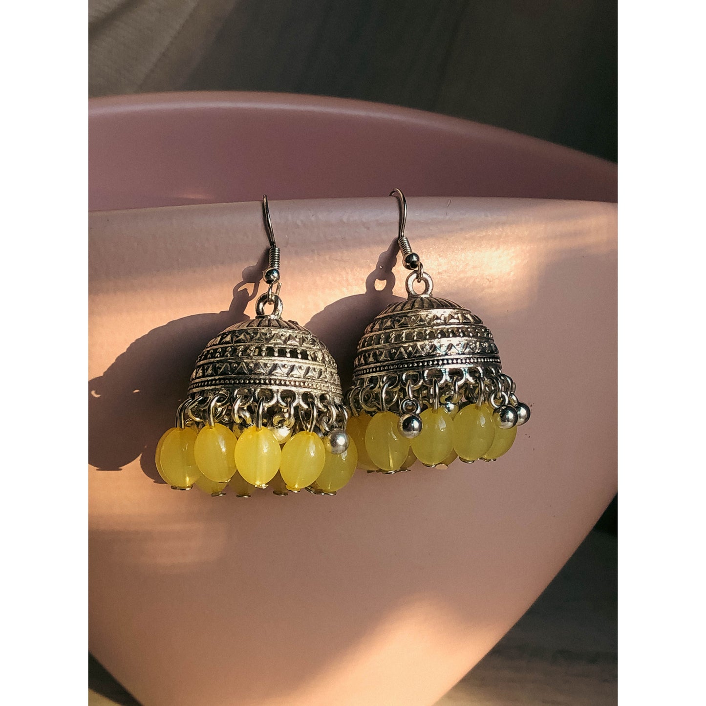 A pair of silver-tone jhumka earrings featuring a round, sparkling top section covered in clear stones, with a bell-shaped dangle below adorned with clear stones and small white pearl or bead accents