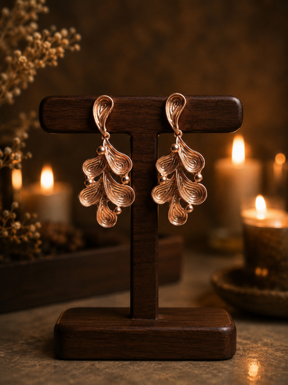 Rose gold leaf-shaped earrings on a wooden stand with candles in the background