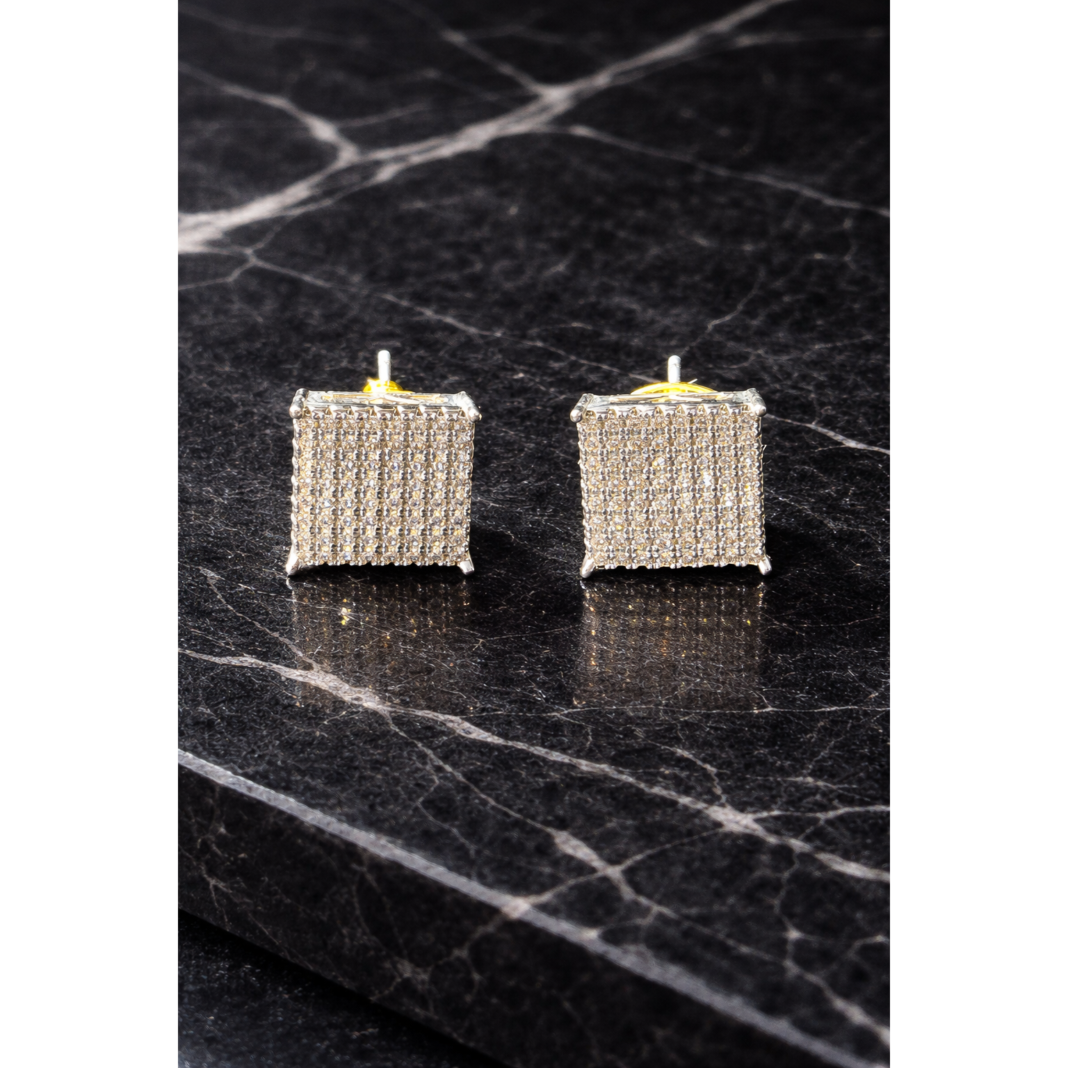 Modern square diamond-style stud earrings on a black marble surface
