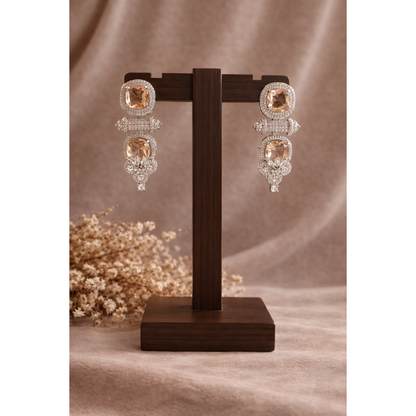 Champagne blush cushion-cut statement drop earrings with pavé halo displayed on wooden stand