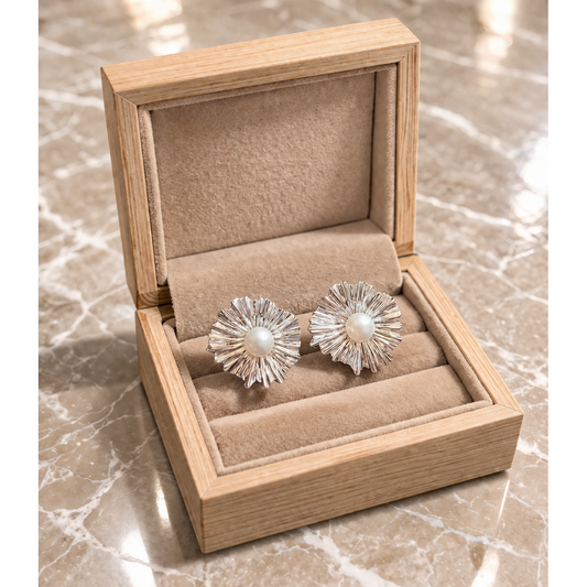 Silver earrings with a pearl center in an open wooden jewelry box on a marble surface
