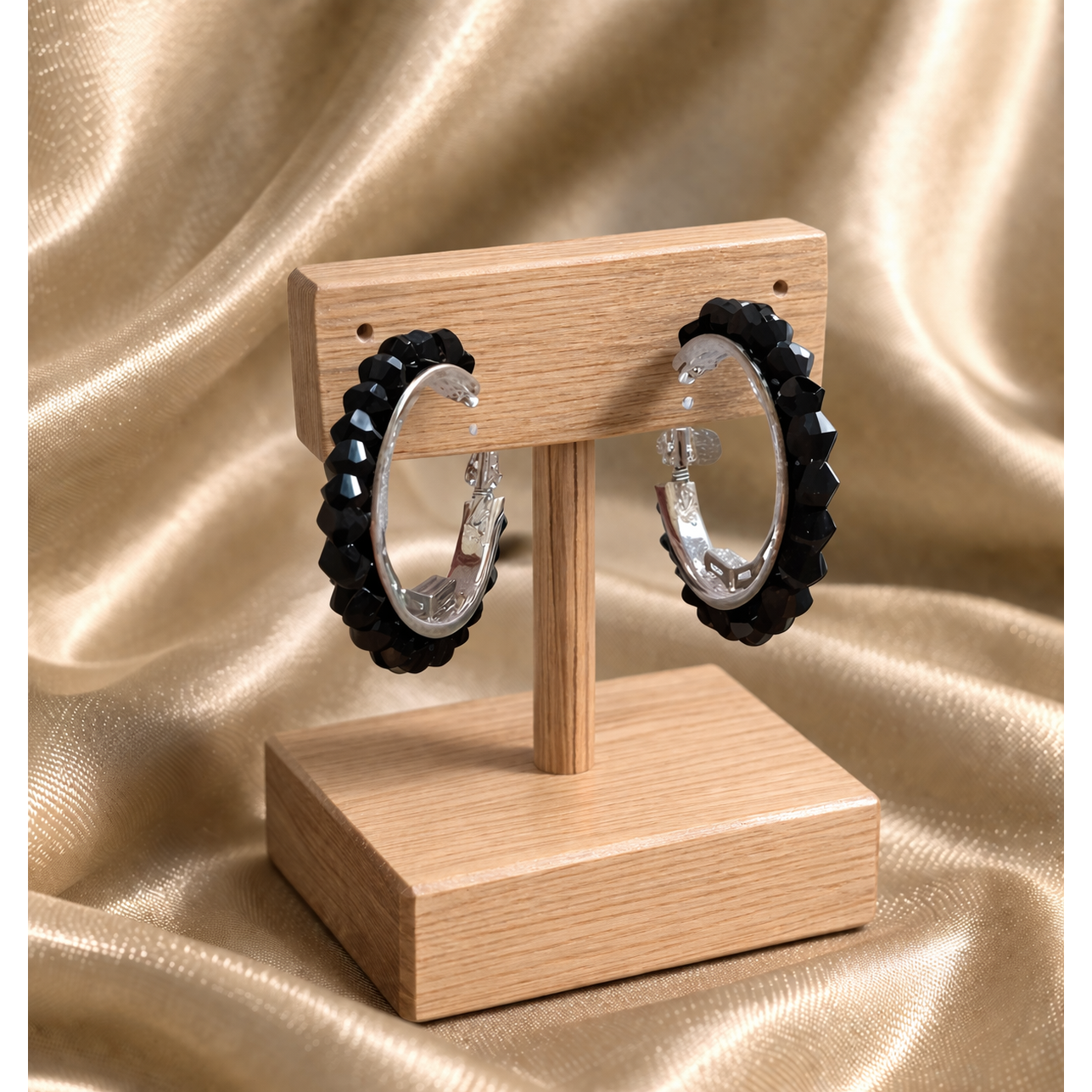 Black beaded hoop earrings on wooden stand with gold satin background