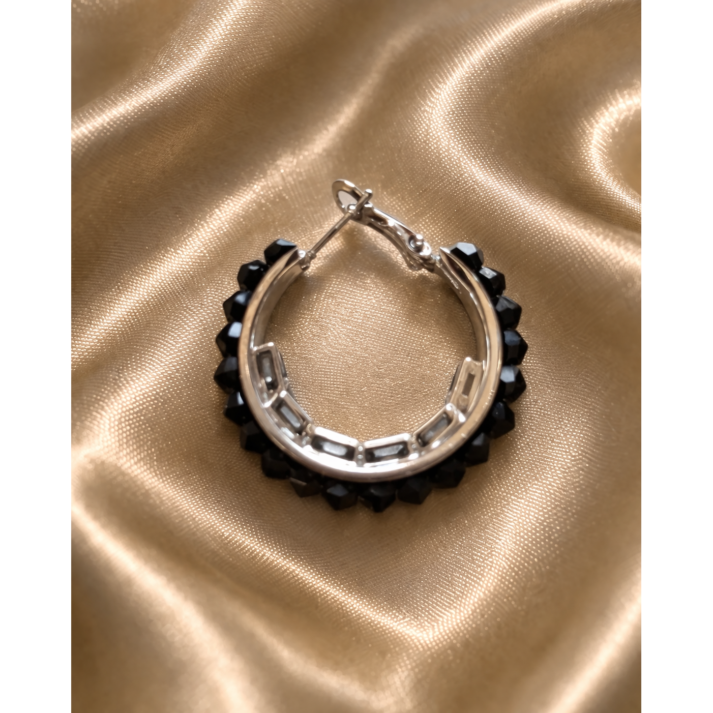 Black crystal beaded hoop earring on gold satin fabric close up