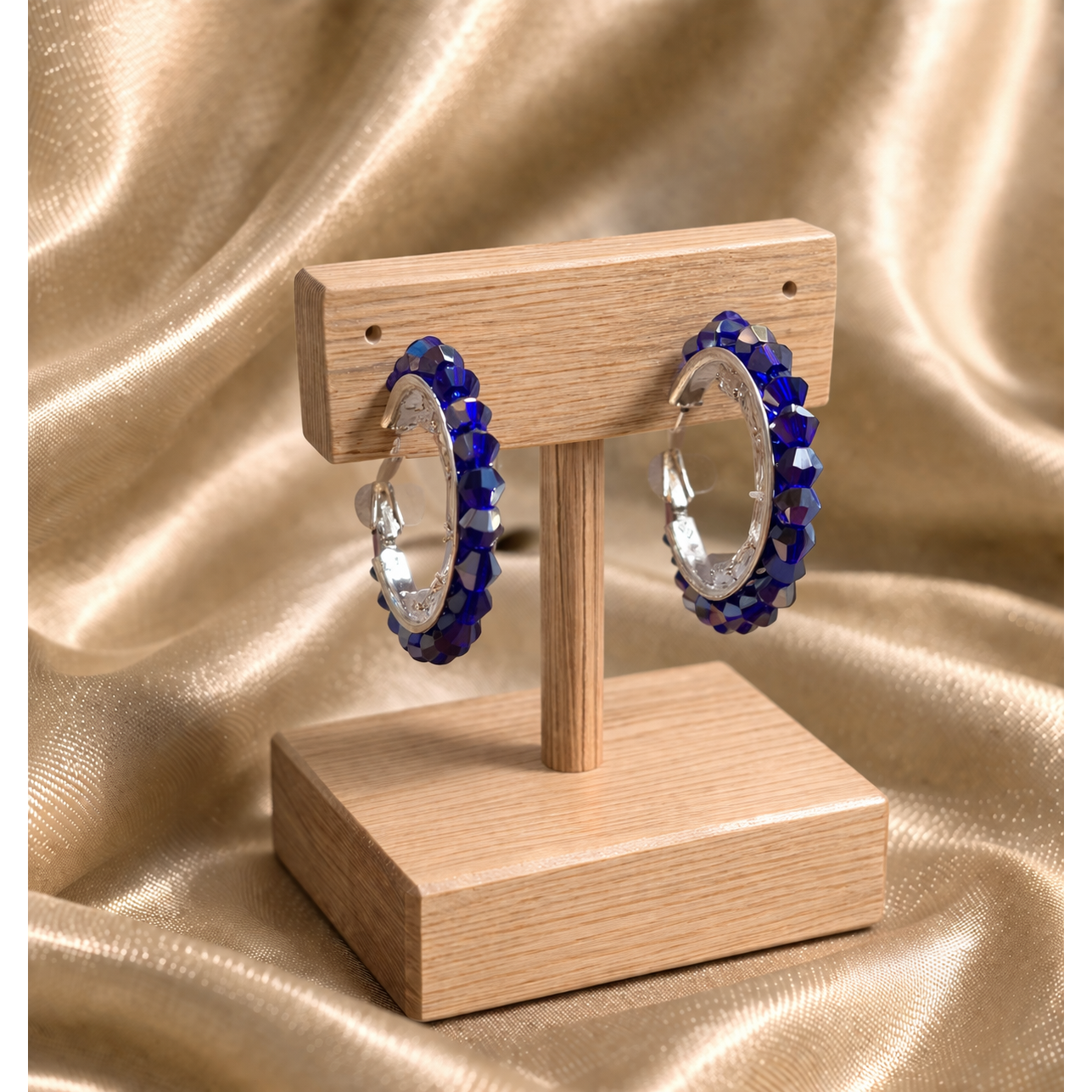 Blue beaded hoop earrings on wooden stand with gold satin background