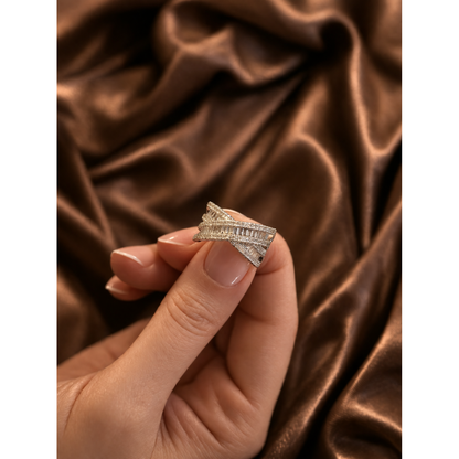 Close-up of adjustable silver multi-layer crisscross ring with baguette and pave stones held in hand against brown satin background