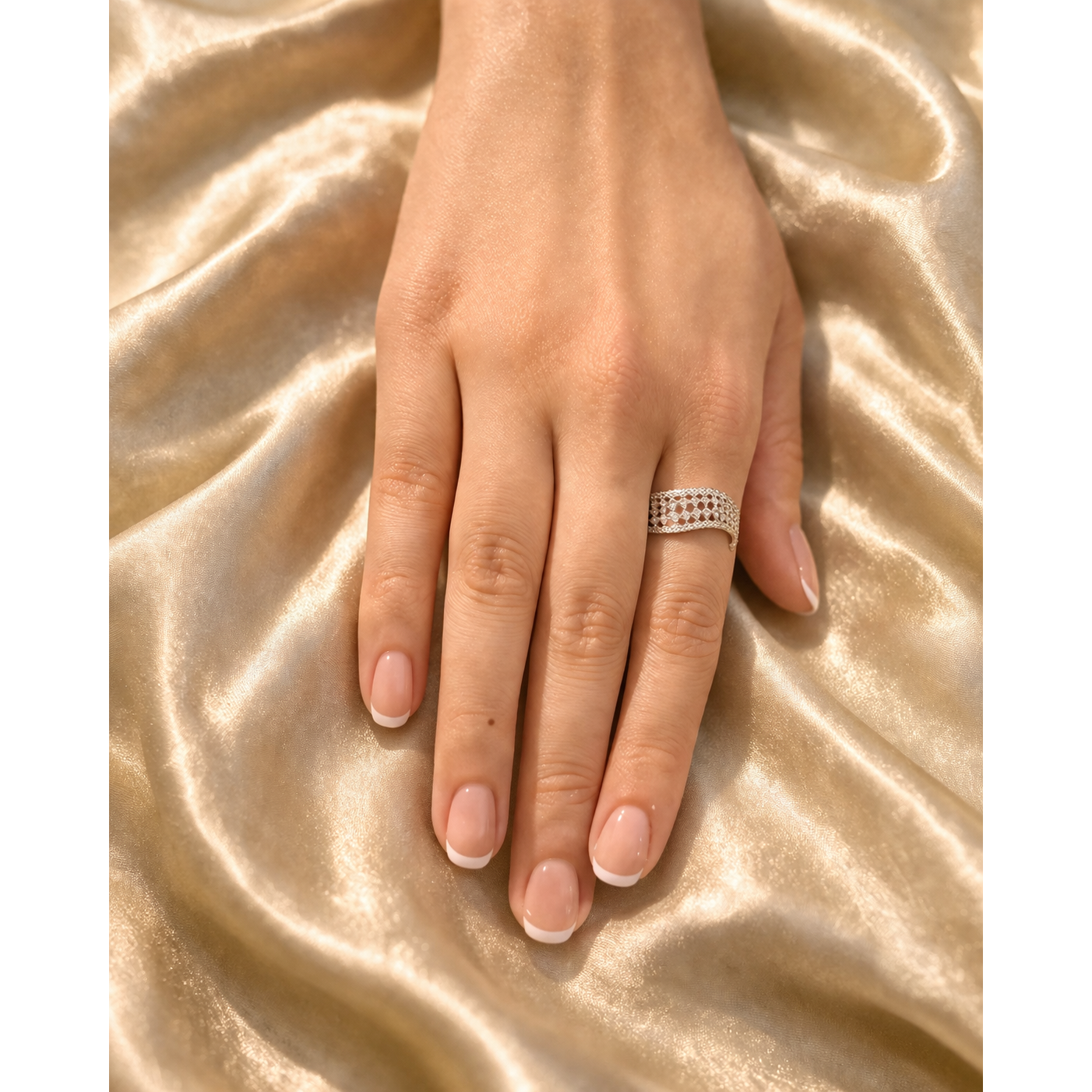 Adjustable silver mesh ring worn on hand over gold satin fabric with soft natural lighting