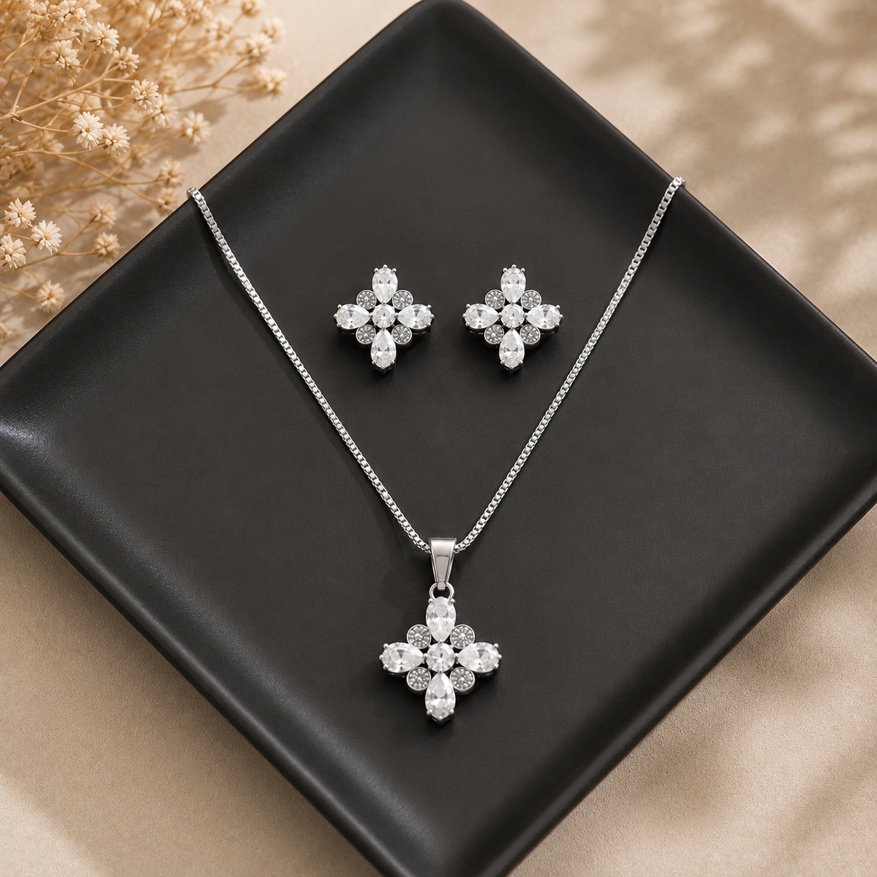 Clear stone silver-tone pendant necklace and matching earrings displayed on a square black ceramic plate.