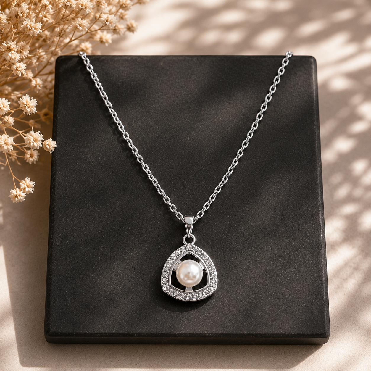 Pearl Axis silver-tone pendant with open triangular frame and clear stone detailing displayed on a black square plate.