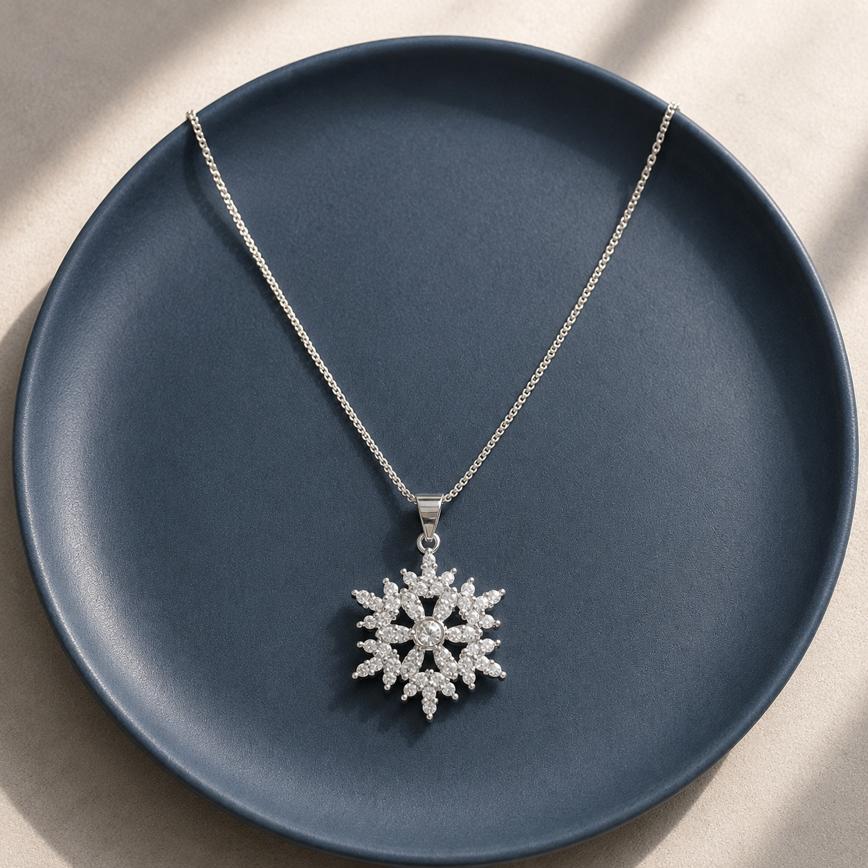 Silver-tone Frost Halo pendant with radiating clear marquise stones displayed on a deep blue ceramic plate.
