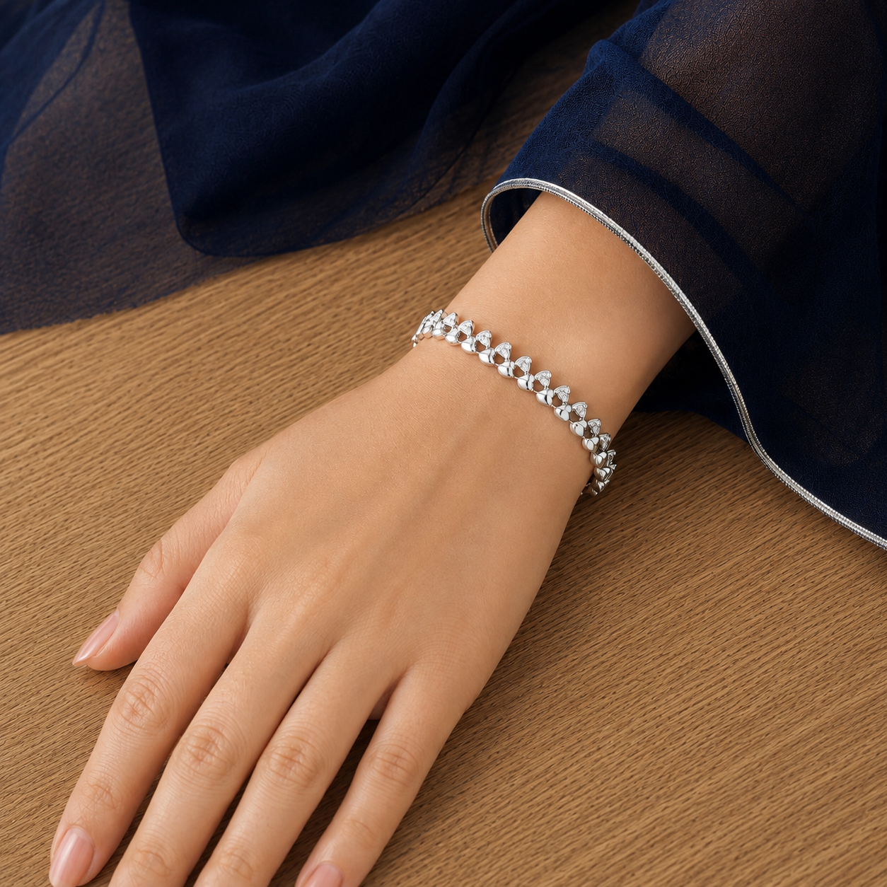 Woman wearing a silver-tone twin-heart bracelet with clear stone accents, resting her hand on a wooden surface.