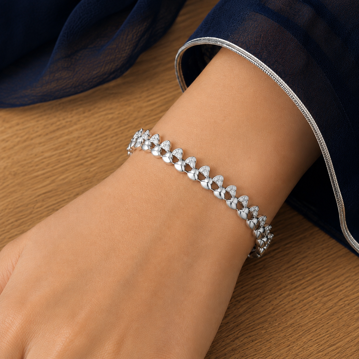 Woman wearing a silver-tone twin-heart bracelet with clear stone accents, resting her hand on a wooden surface.