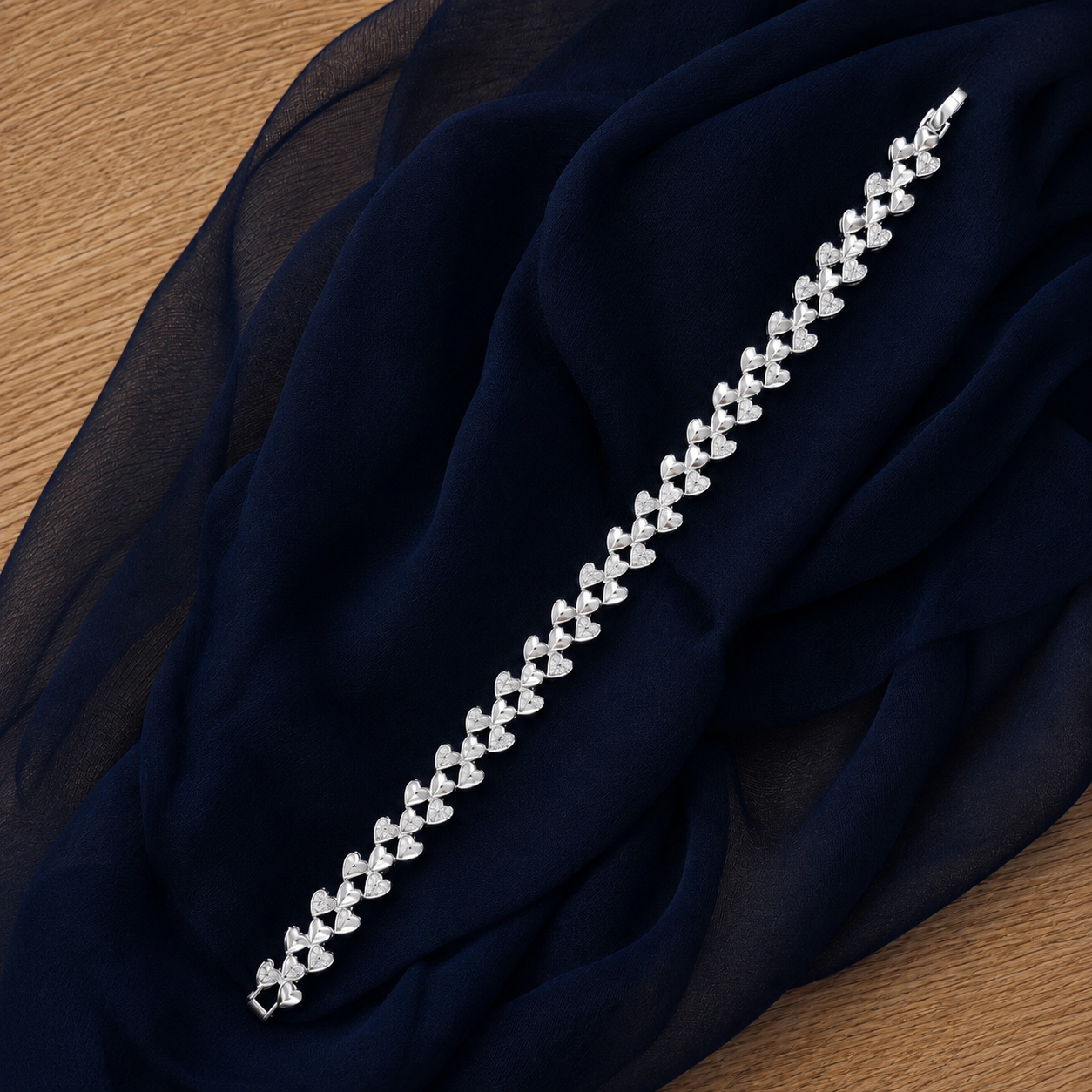 Silver-tone Twinheart Line Bracelet with alternating polished and clear stone-set heart links displayed on navy chiffon.