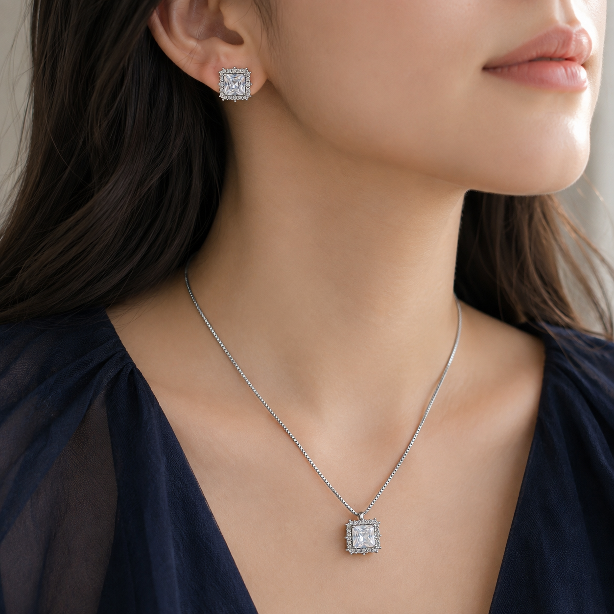 Model wearing Lucent Frame silver square pendant necklace and matching square zircon earrings with a navy outfit.