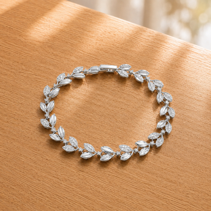 Silver leaf-link bracelet displayed in a circular arrangement on a light oakwood surface, highlighting its polished and zircon-detailed design.