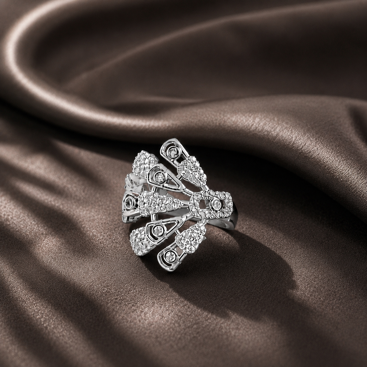 Close-up of silver zircon statement ring displayed on dark brown satin with sculpted openwork and radiating details.