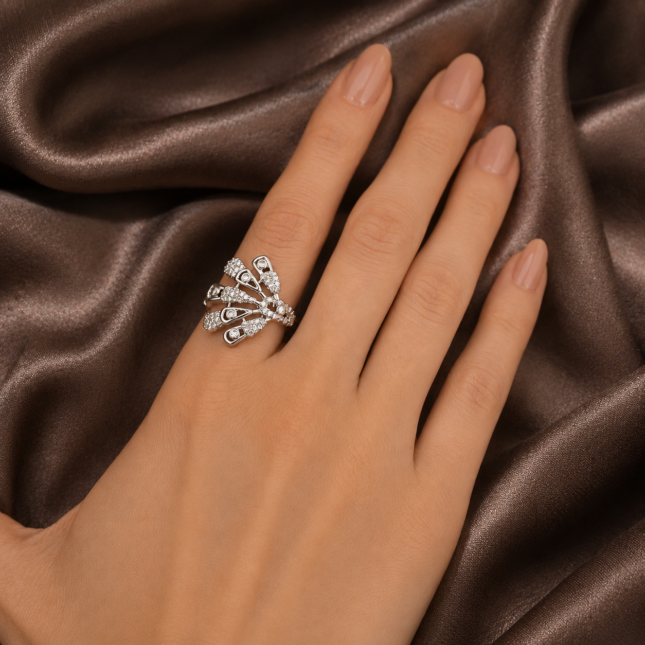 Silver Radiant Rift statement ring worn on a manicured hand against rich brown satin, showing its asymmetric zircon fan desig