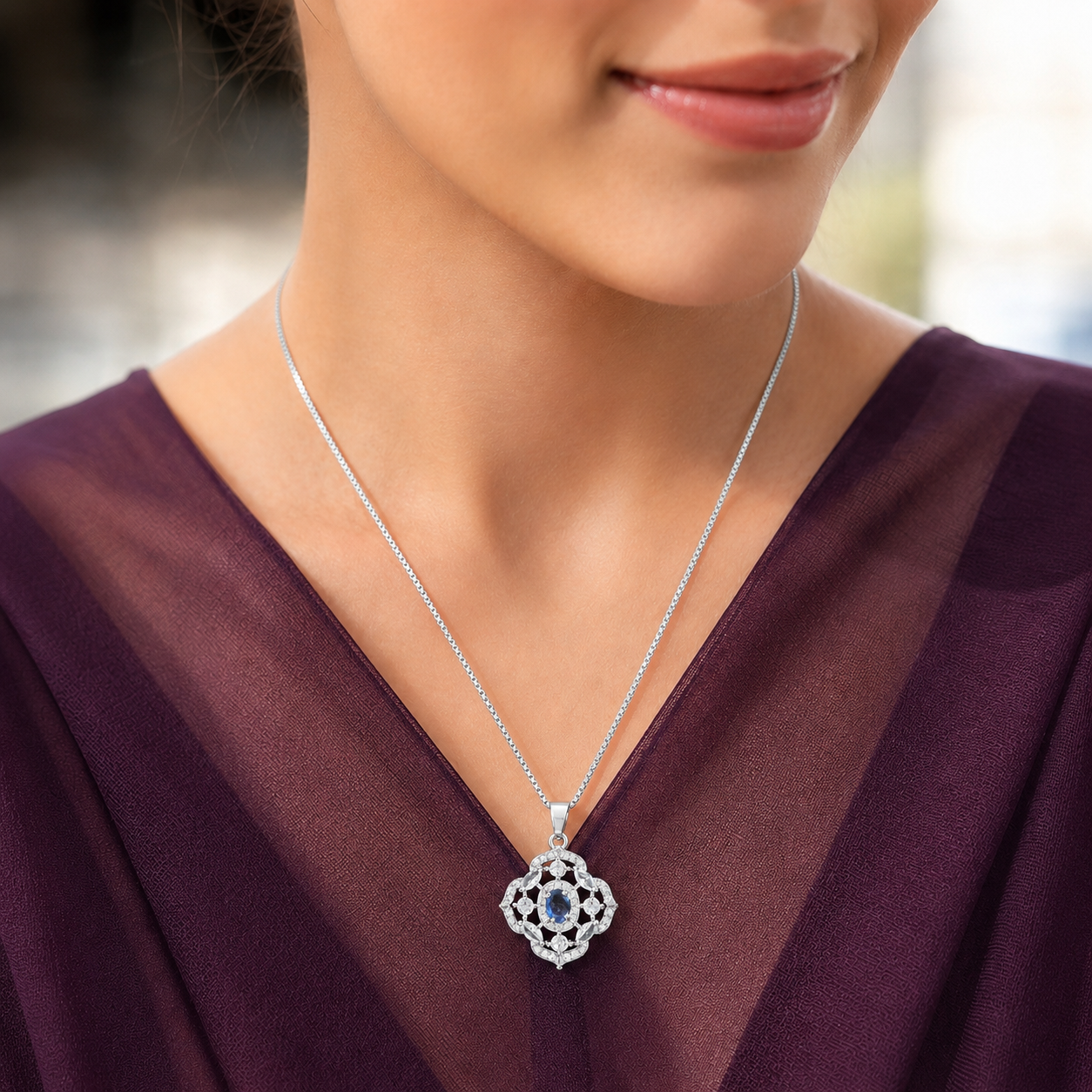Model wearing a small silver-tone blue stone locket with clear zircon accents against a deep plum outfit.
