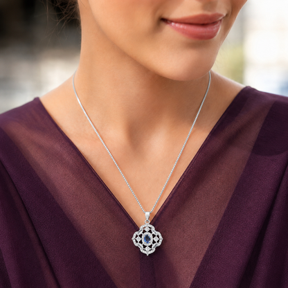 Model wearing a small silver-tone blue stone locket with clear zircon accents against a deep plum outfit.