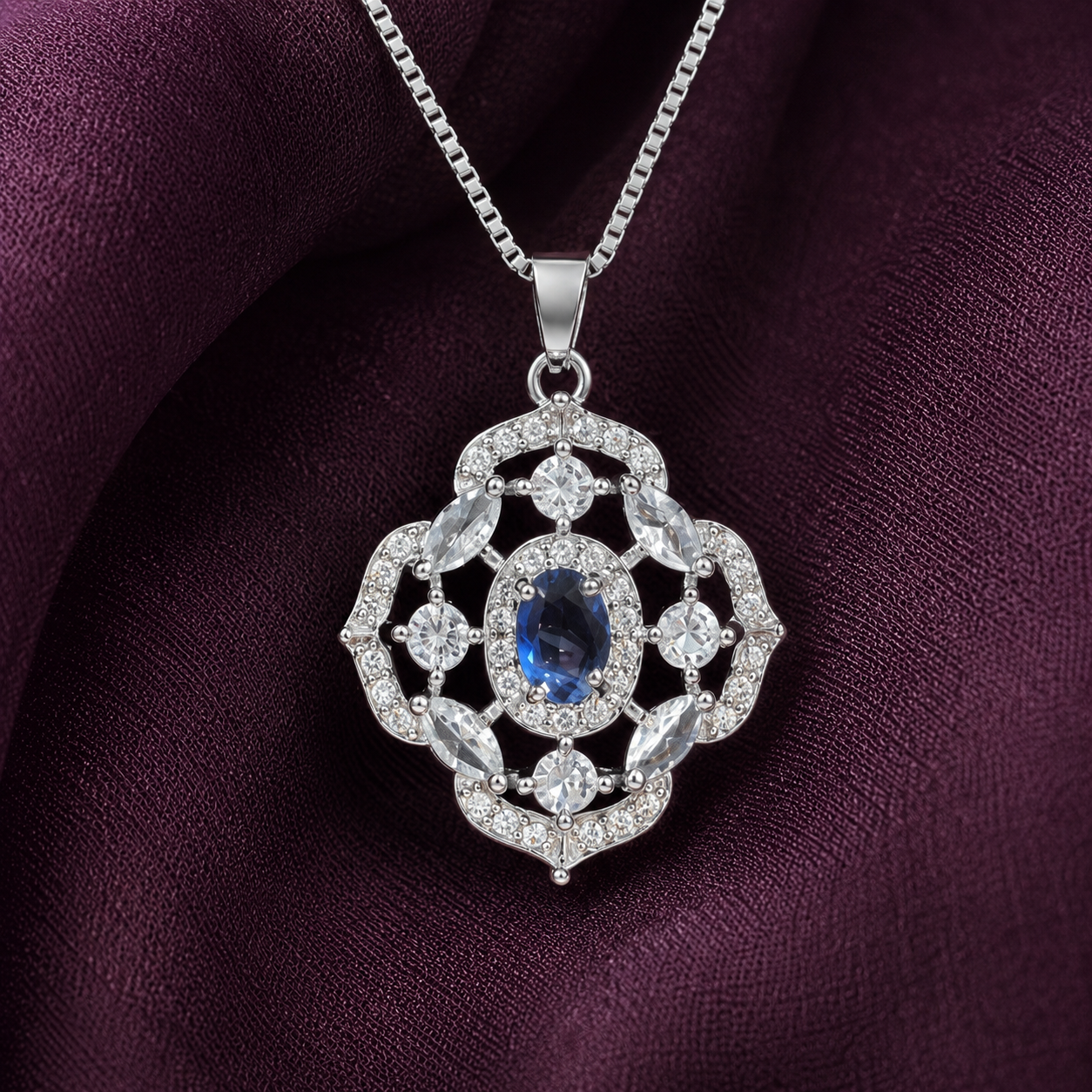 Close-up of intricate silver locket featuring a blue oval centre stone, marquise-cut clear accents and zircon-studded openwork detailing.