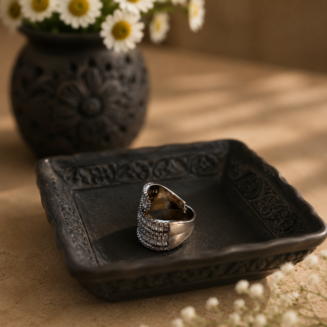 Side profile of an S925 sterling silver wrap ring with layered baguette zircon detailing presented on a black carved ceramic plate in warm natural light