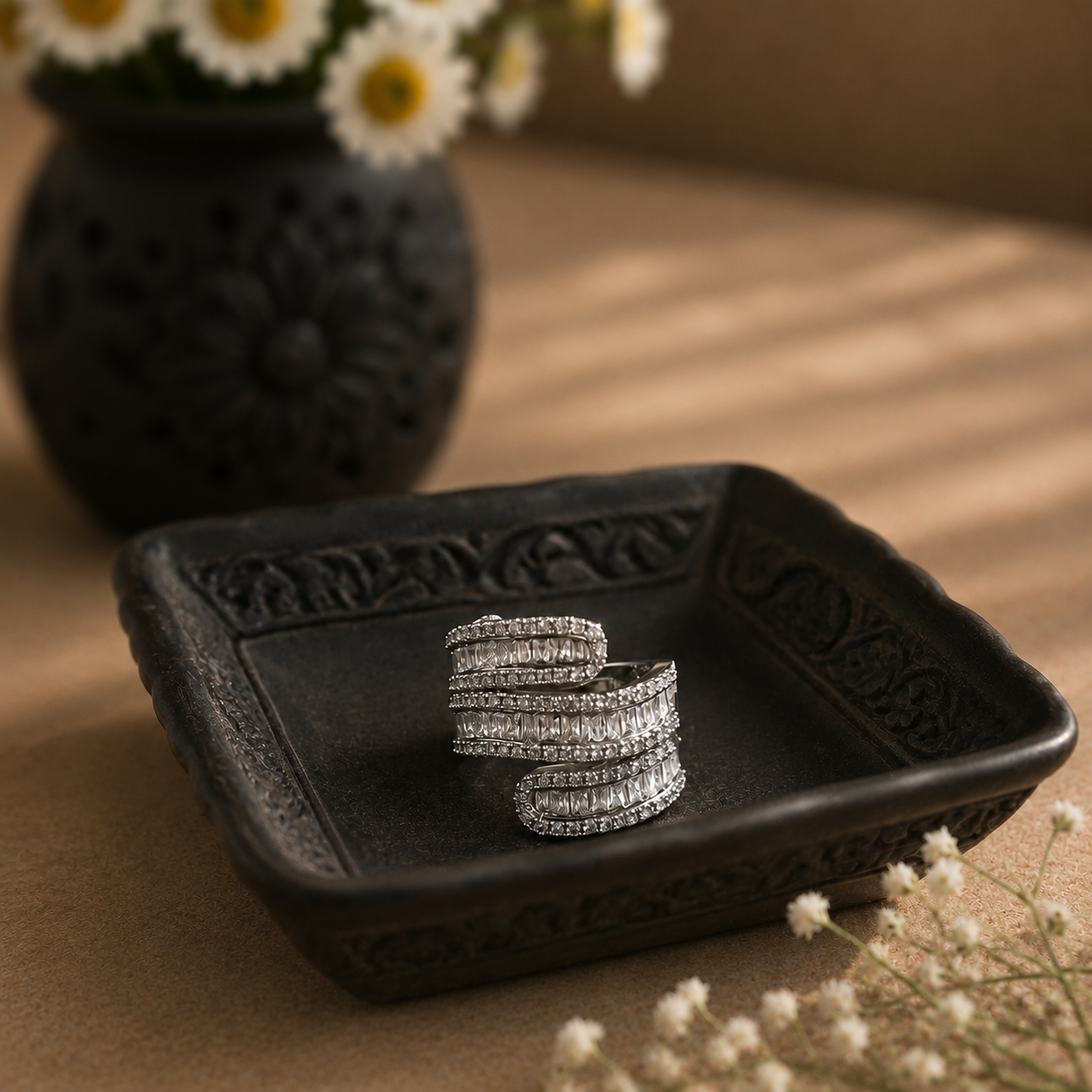 S925 sterling silver multi-row wrap ring displayed on a black carved ceramic square plate with a softly blurred daisy vase in the background