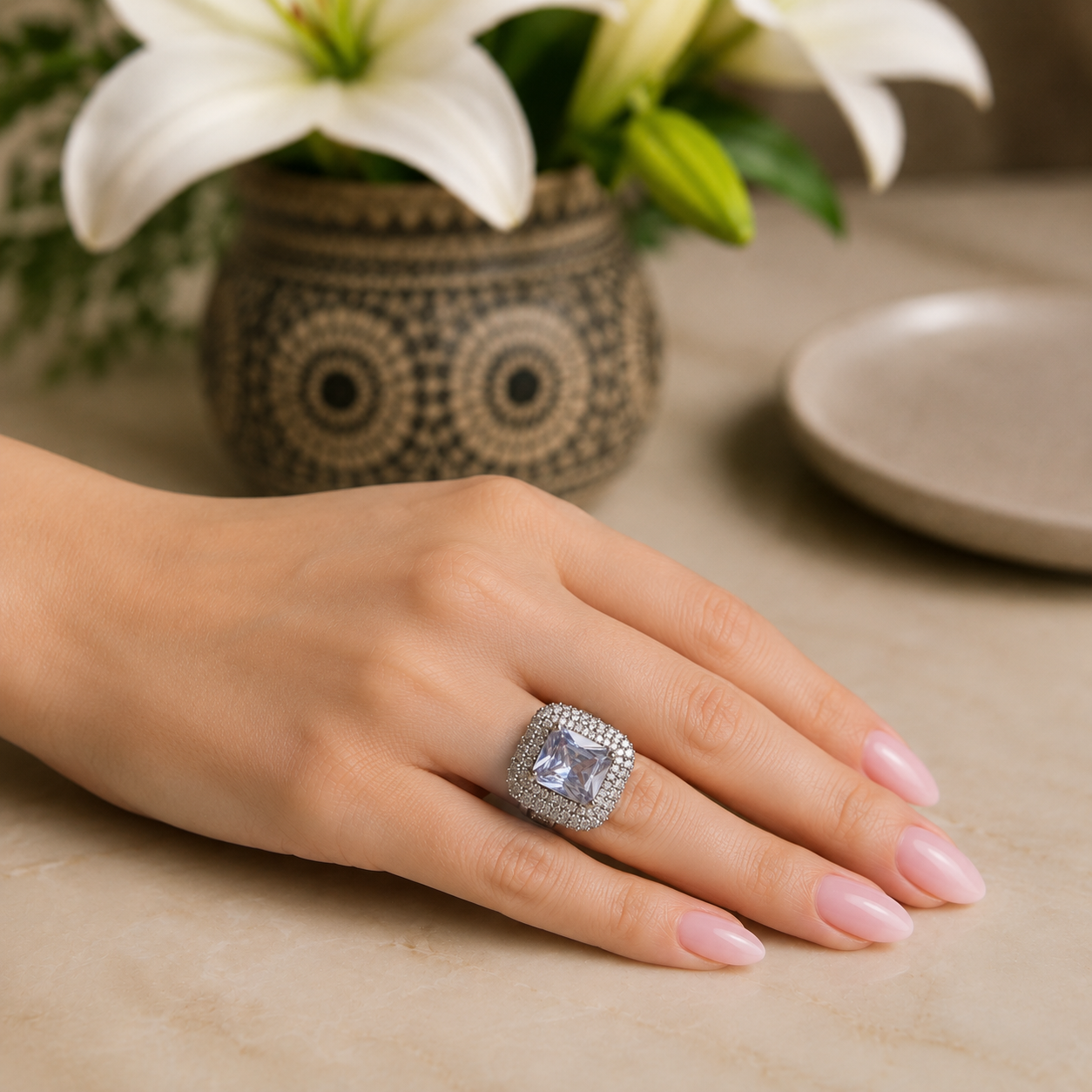 Clear cushion-cut statement ring worn on a hand with soft pink nails, photographed in natural daylight.