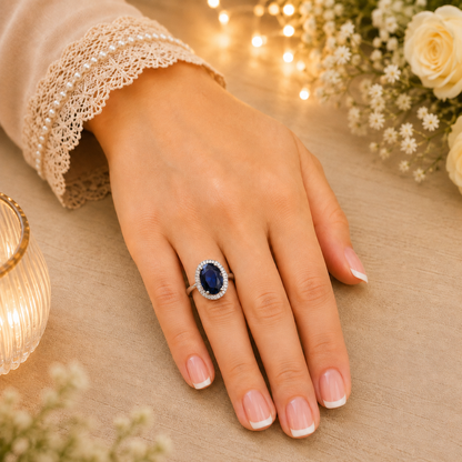
Deep blue oval halo ring worn on a hand with French manicure in a warm luxury lifestyle setting.