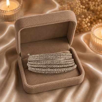 Multi-row crystal spring bracelet displayed inside a soft taupe velvet jewelry box on champagne satin with candles and dried flowers.