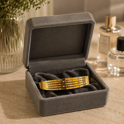 Gold-tone crystal line bracelet for thinner wrists displayed inside a premium grey velvet jewelry box on a travertine dressing table with softly blurred perfume bottles and floral décor.