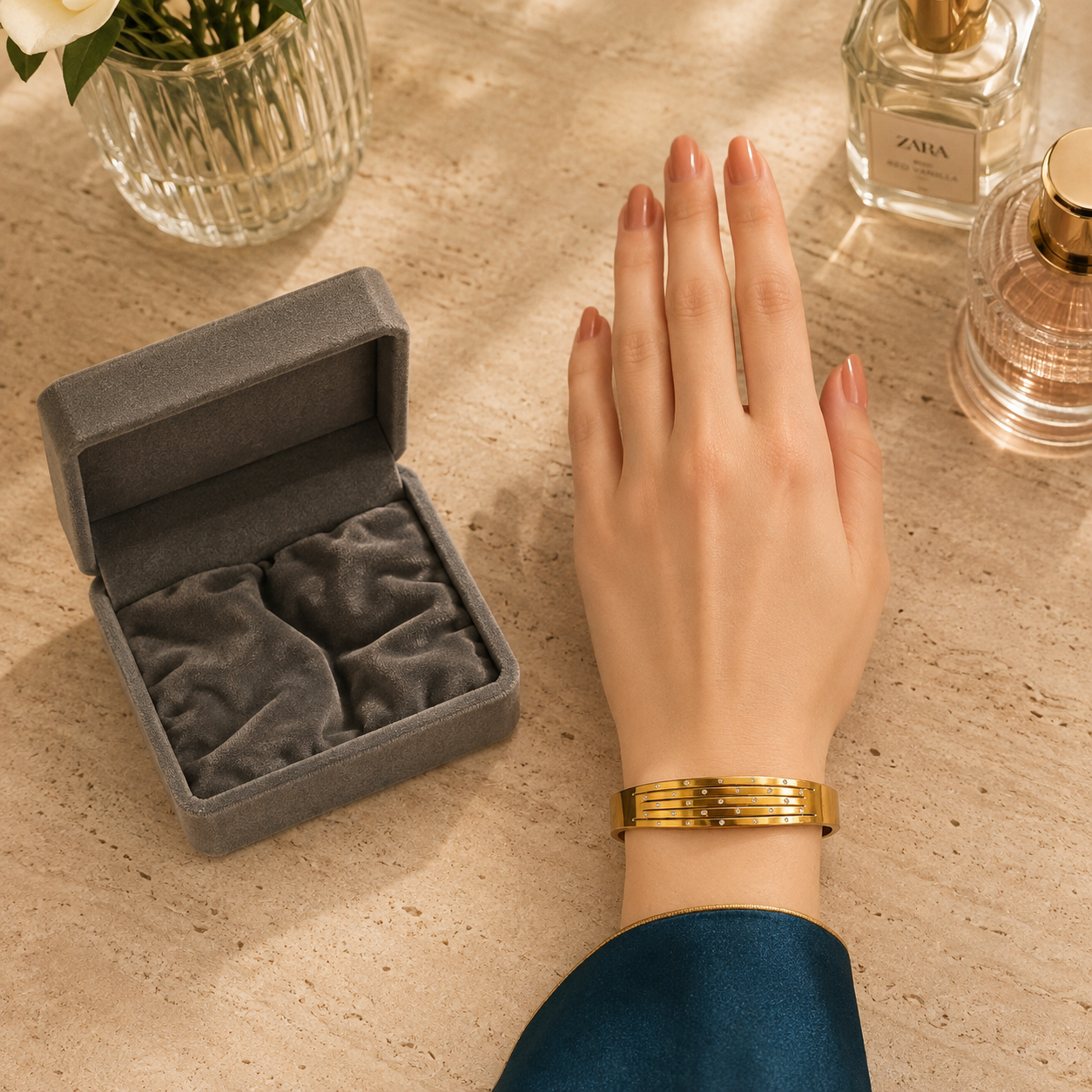 Gold-tone crystal line bracelet designed for thinner wrists, worn on a hand beside an open grey velvet jewelry box on a luxury travertine dressing table