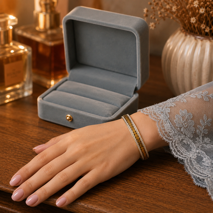 Gold crystal cuff bracelet worn on a hand with soft pink nails beside a premium velvet jewelry box on a wooden dressing table.