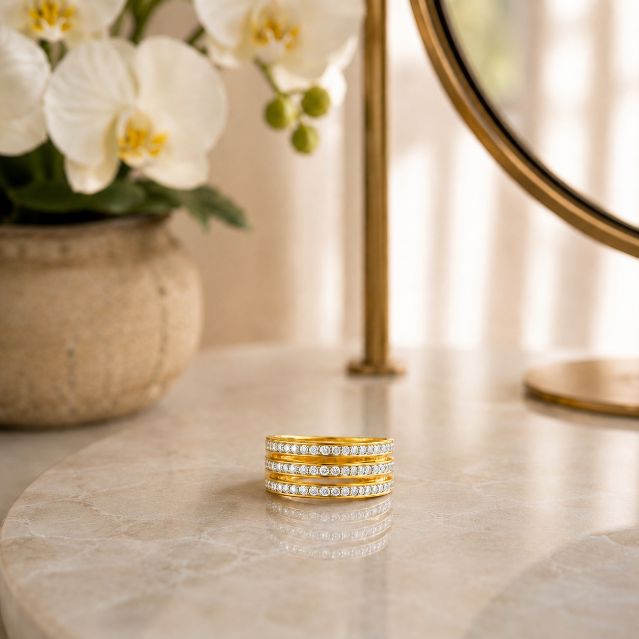 Light gold stainless steel wide band ring with three rows of clear crystals displayed on reflective marble