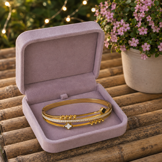 Gold lock bracelet with black and white clover accents displayed inside a blush velvet jewellery box.