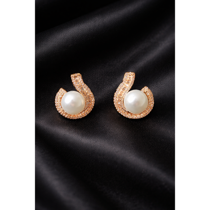 Luxury TIAS gold pearl stud earrings with sparkling crystal accents placed on fine black satin fabric.