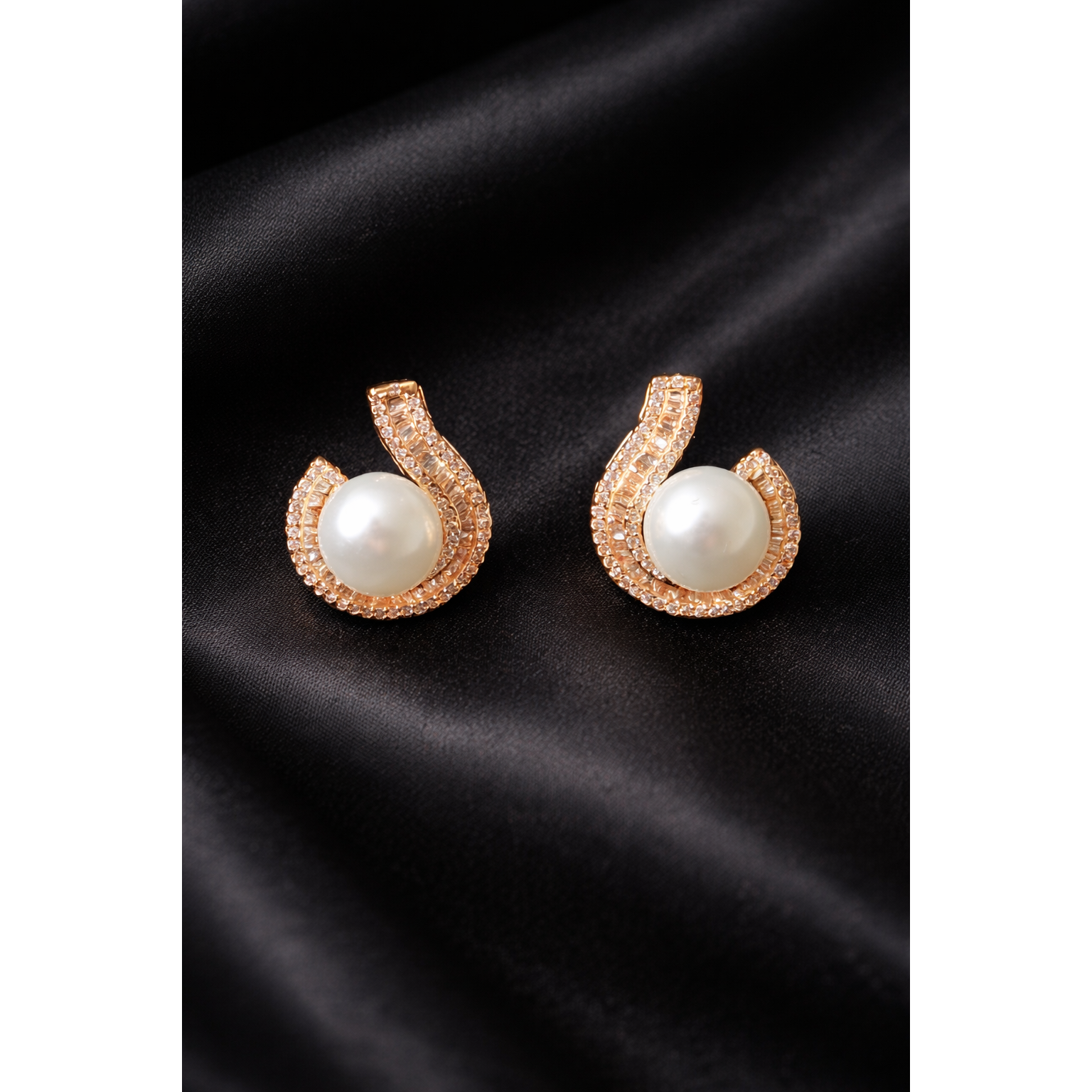TIAS gold pearl stud earrings with crystal accents displayed on a black satin fabric
