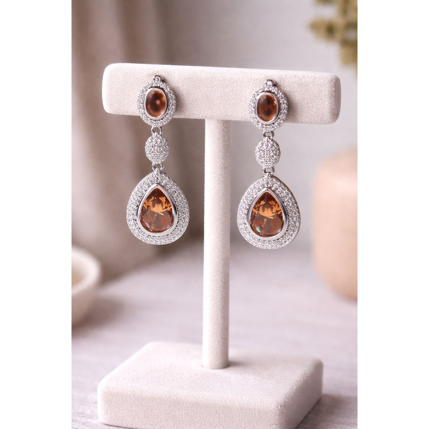 High-definition product photo of silver drop earrings with bronze crystal stones displayed on a jewelry stand, featuring pavé detailing and a modern statement design.