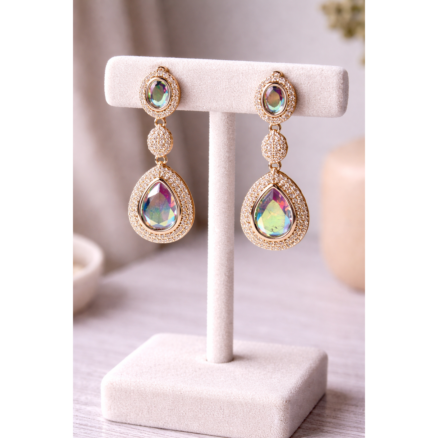 Light gold drop earrings with iridescent crystal stones on a jewelry stand, showcasing pavé accents and a colour-shifting statement style.