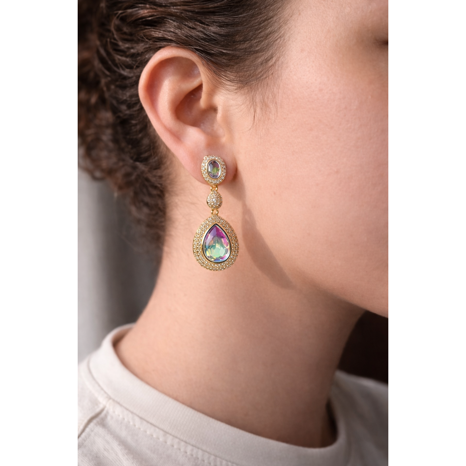Model wearing light gold drop earrings with iridescent crystals, highlighting iridescent colours and pavé detailing in a high-fashion jewelry style.