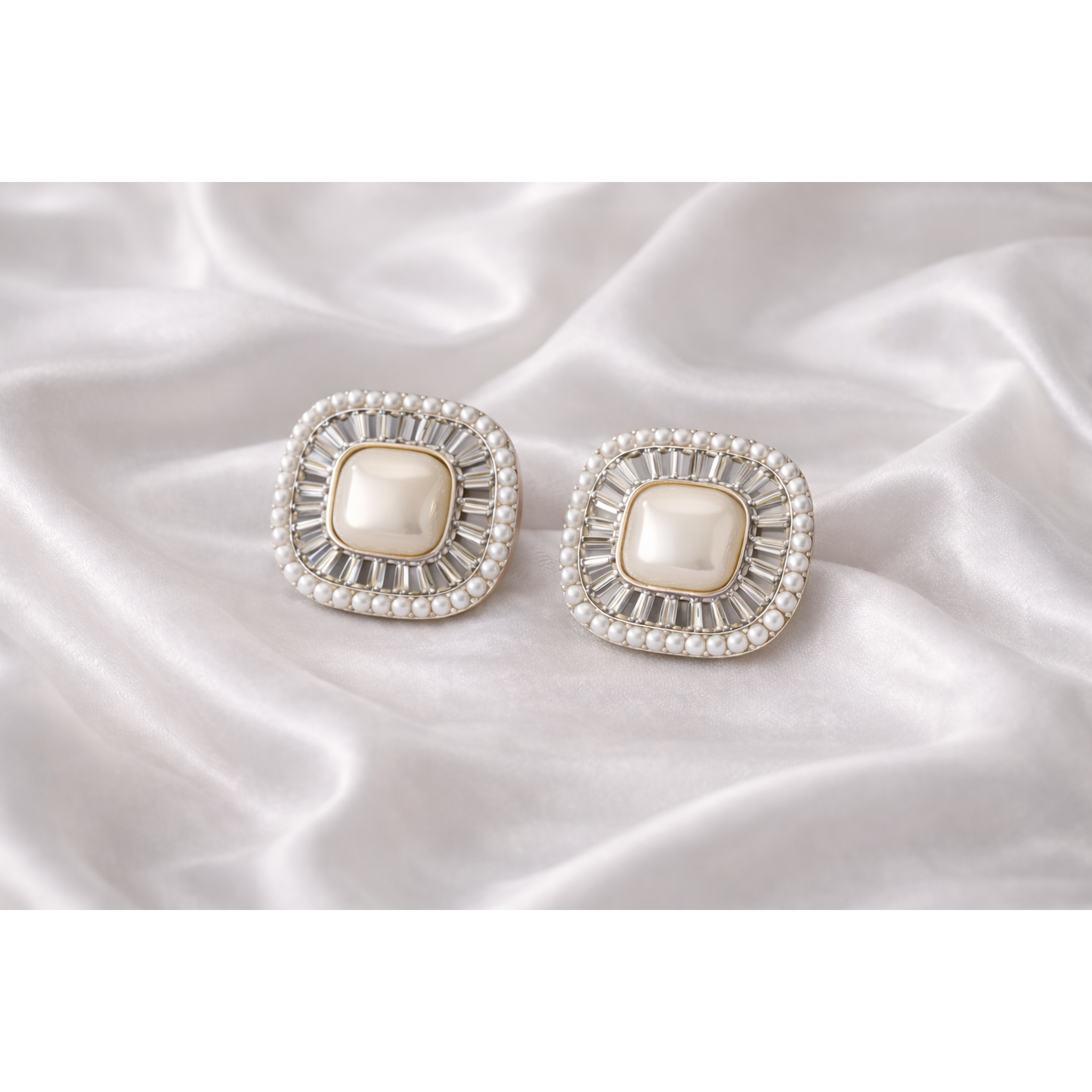 Square pearl halo stud earrings placed on white silk fabric showing crystal detailing and micro pearl border in high definition