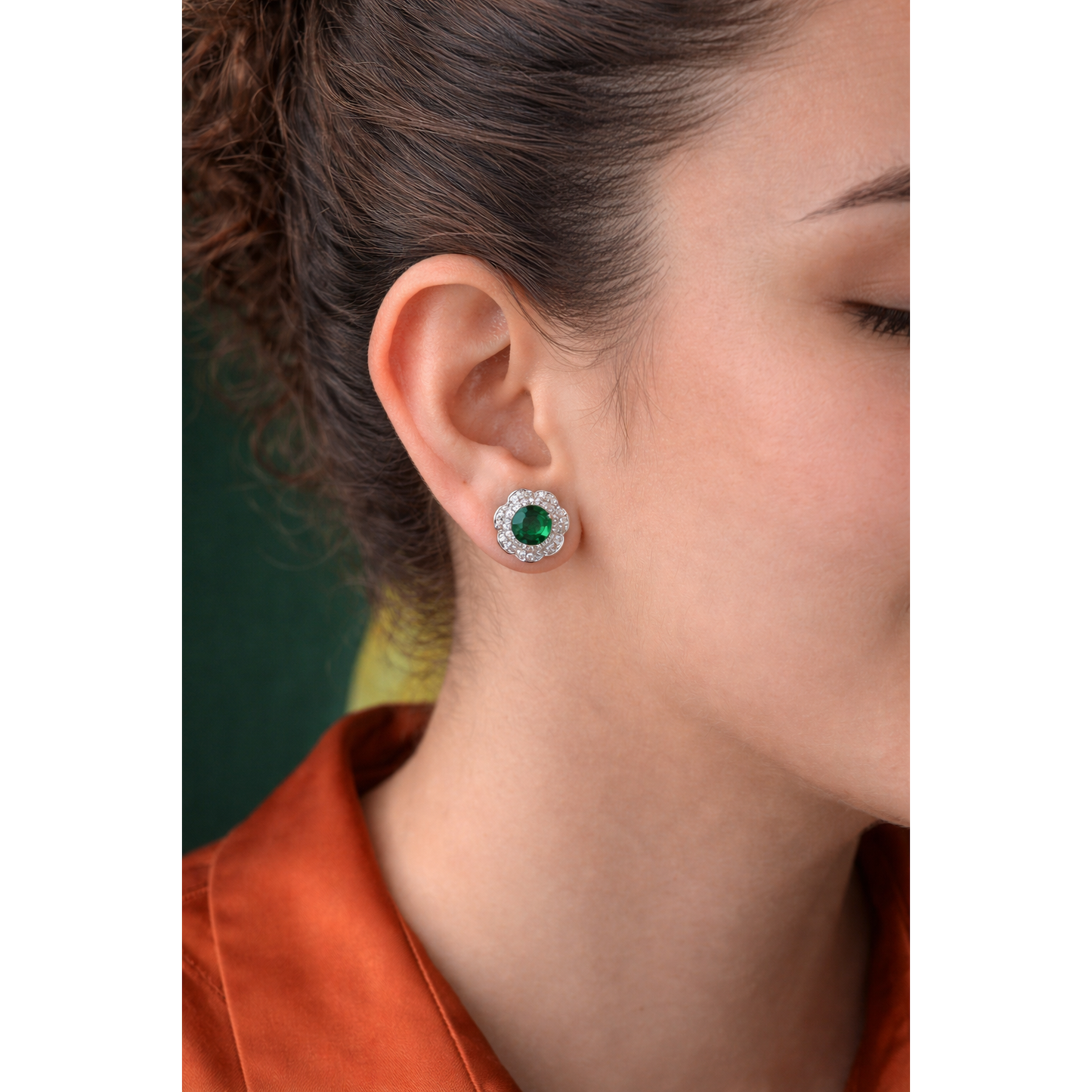 Close-up of woman wearing silver floral halo stud earrings with green centre stone, side profile jewellery shot