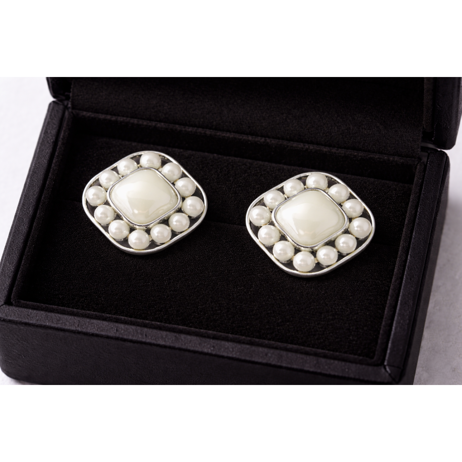 Silver pearl square stud earrings with mother-of-pearl center displayed inside a black velvet jewellery box, high-definition product photography.