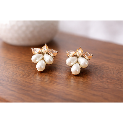 Creamy pearl cluster stud earrings placed on a fine wooden surface with blurred ceramic vase in background, high-definition jewellery product image.