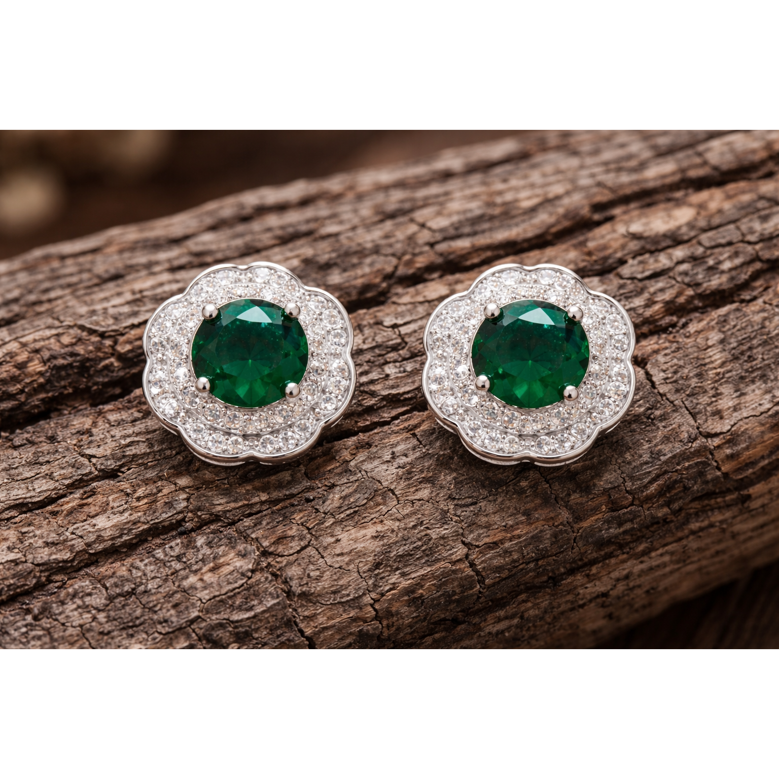 Silver floral halo stud earrings with emerald green centre stones photographed on textured wood